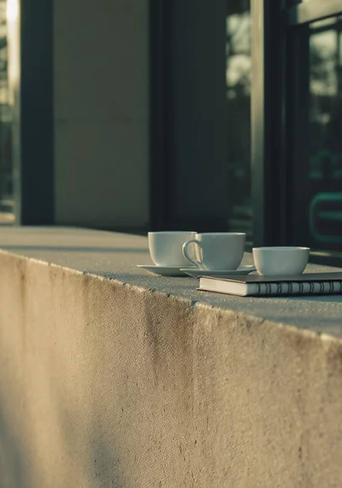 Twee koppen koffie en een notitieboek op een betonnen rand bij de ingang van een gebouw