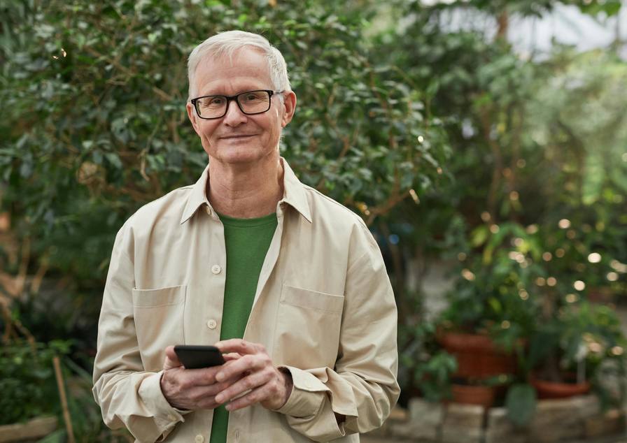 Man met bril en een telefoon in zijn handen, tussen de planten in een kas